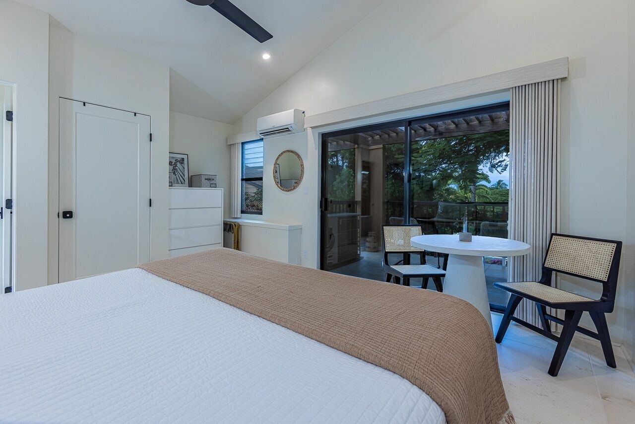 A bedroom with a large bed, a desk, and a chair near a sliding glass door leading to an outdoor area with a table and chairs.