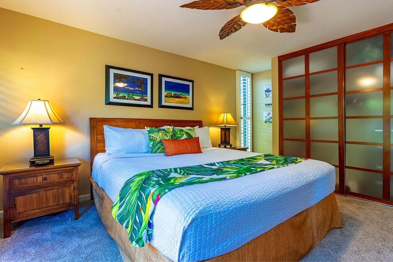 A bedroom with a wooden bed, two bedside lamps, a nightstand, a ceiling fan, and two framed pictures on the wall.