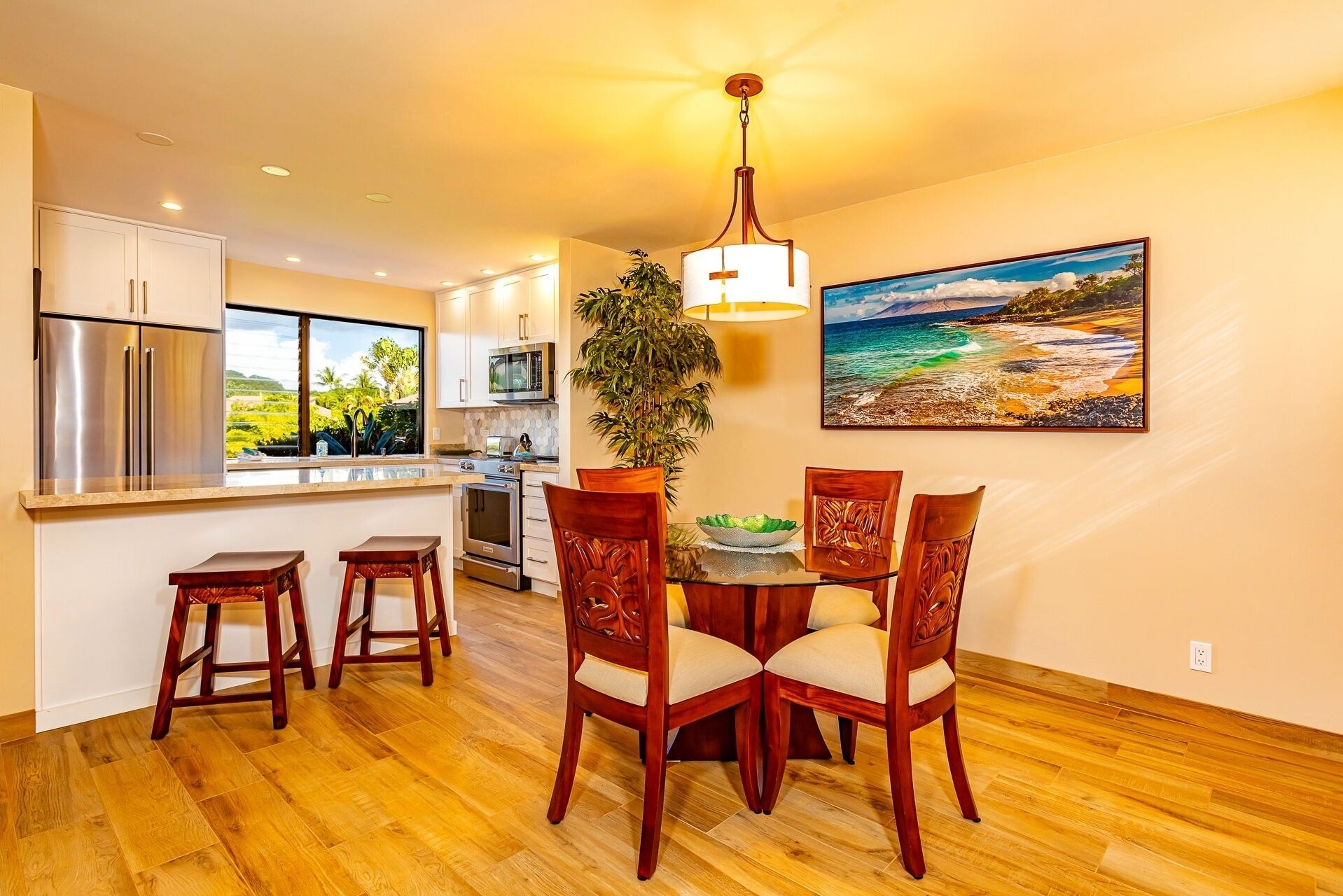 A modern kitchen with stainless steel appliances, a dining area with wooden chairs, and a large window offering a view of greenery.