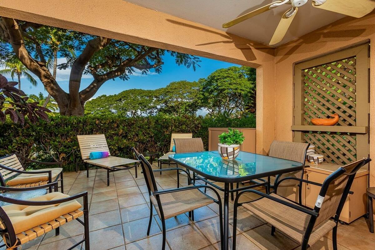 Eine Terrasse im Freien mit einem Glastisch und Stühlen, umgeben von üppiger Vegetation und einem großen Baum.