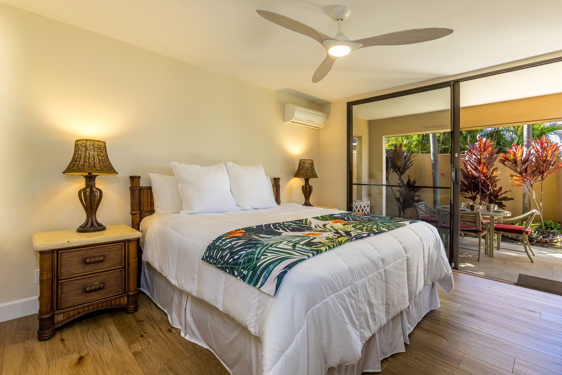 A bedroom with a bed, two bedside tables with lamps, a ceiling fan, and an air conditioning unit.