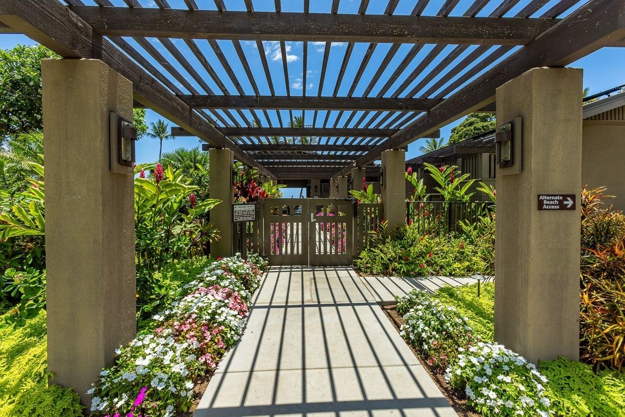 A covered walkway with a gate, surrounded by lush greenery and flowering plants.