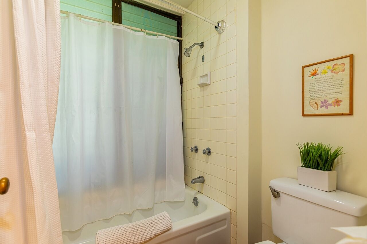 Een badkamer met douchegordijn, toilet, wastafel en een tekst in een lijst op de muur.