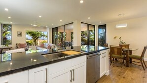 Una cocina moderna con una isla central, muebles blancos y vistas al exterior gracias a amplias ventanas.