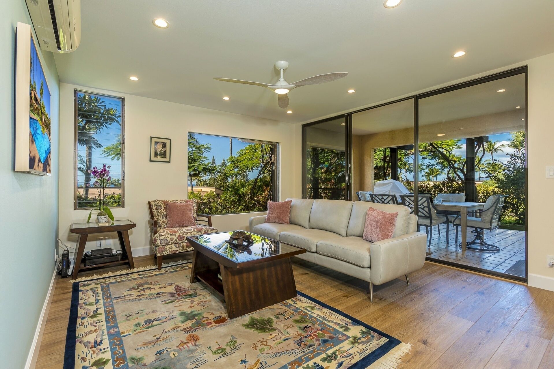 Un salon spacieux avec un grand canapé, une table basse et un coin repas comprenant une table et des chaises. De grandes fenêtres offrent une vue sur la verdure, et un balcon est également présent.