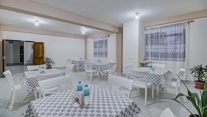 A dining area with multiple tables and chairs, each with a checkered tablecloth. There are potted plants and a sink visible in the background. - Treebo Staying Center (Shillong)