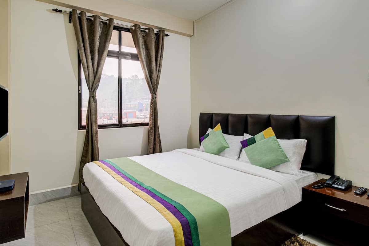 Habitación de hotel con cama, televisor de pantalla plana montado en la pared, mesita de noche con teléfono y ventana con cortinas.
