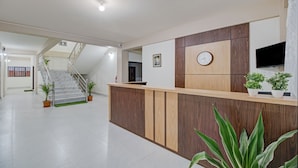 A reception area with a wooden reception desk, a clock, and potted plants. - Treebo Staying Center (Shillong)