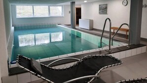 En inomhuspool med klart vatten, några solstolar och en bänk.