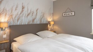 Ett sovrum med en säng, två sänglampor, en väggmonterad skylt med texten ”BEACH” och en vägg med ett mönster som liknar gräs.