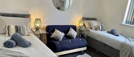 A modern bedroom with a sofa bed, two single beds, a mirror, and a window.