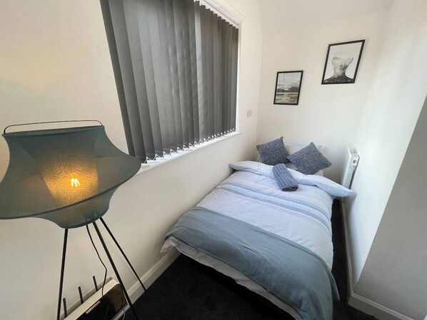 Une petite chambre à coucher, bien rangée, avec un lit, une chaise et une fenêtre équipée de stores.