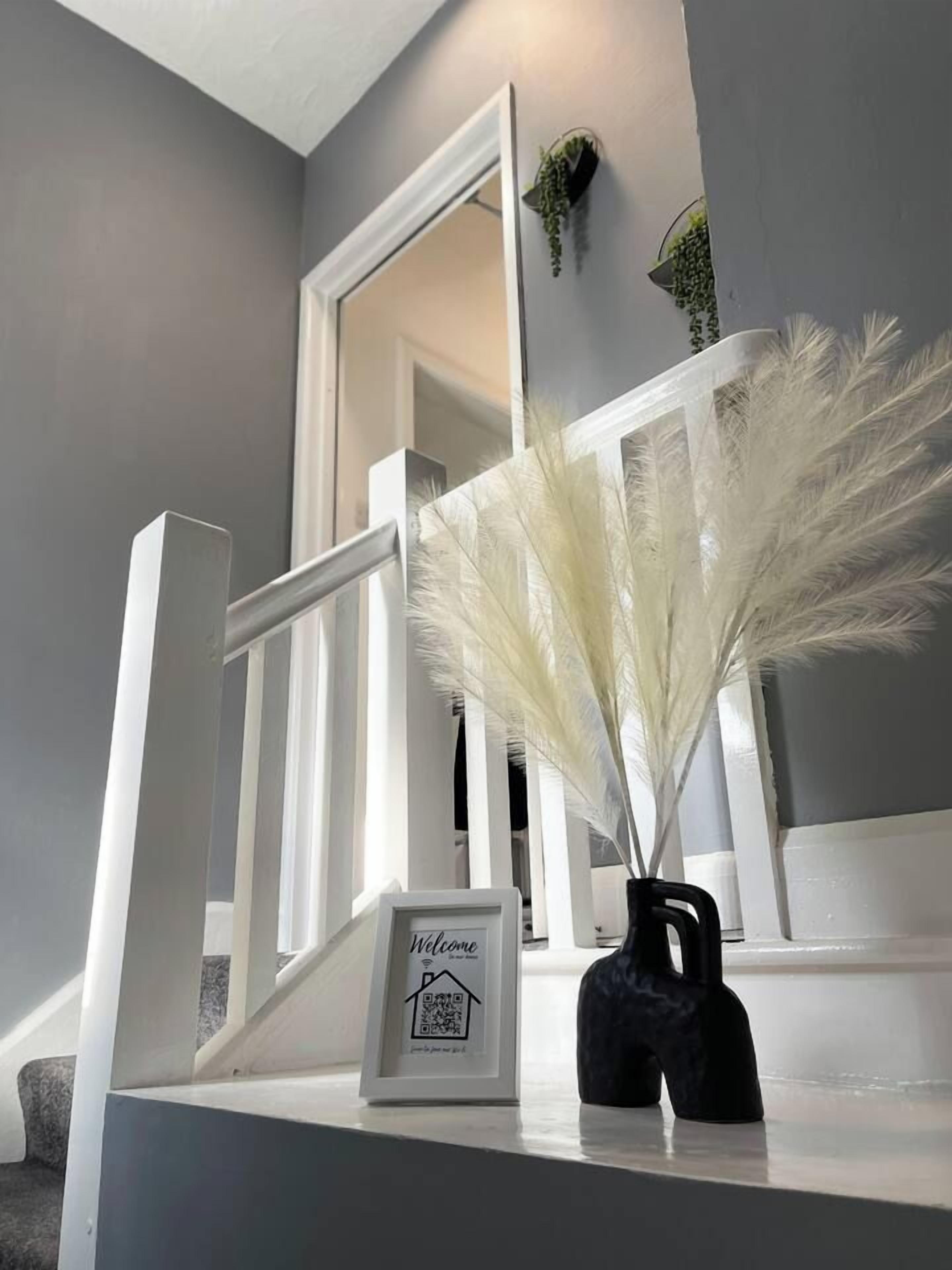Un escalier avec des rampes blanches, une pancarte de bienvenue et un vase rempli de fleurs blanches.
