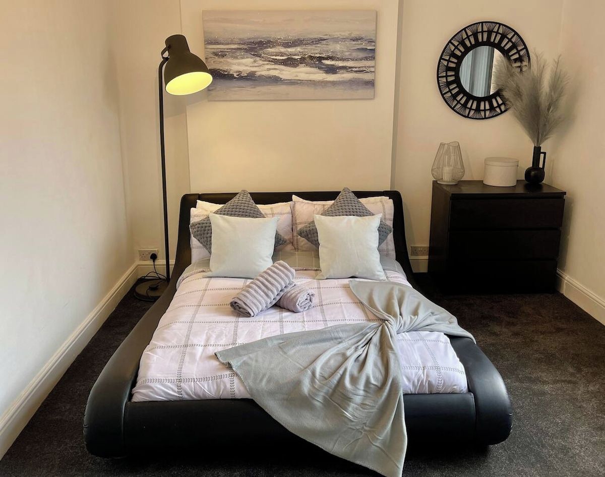 Un letto rifatto con una testiera, una lampada da comodino, uno specchio fissato alla parete e un tavolino con oggetti decorativi.