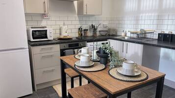 Une cuisine moderne avec des meubles blancs, un plan de travail noir et une table à manger en bois agrémentée de sets de table en fibres tressées.
