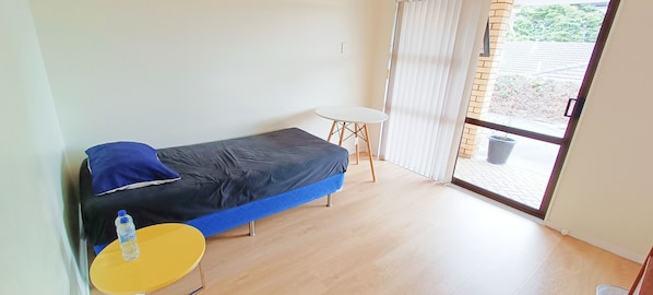 A small room with a single bed, a small table, and a window with a view of the outside.