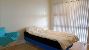 Un dormitorio con una cama, una silla azul y una ventana con persianas.