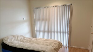 Un dormitorio con cama, ventana con persianas y suelo de madera.