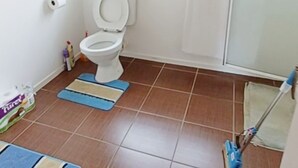 Un baño con inodoro, ventana, ducha y escoba.