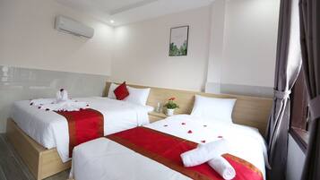 A hotel room with two beds, each with white bedding and red accents, a small plant on the nightstand, and a framed picture on the wall.