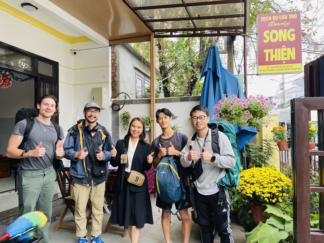 A group of people standing in a covered outdoor area with a signboard in the background.