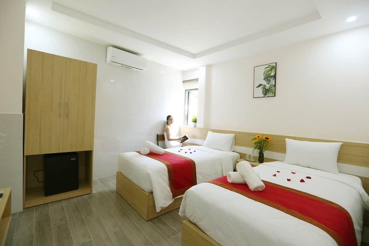 A hotel room with two beds, a minibar, a wooden wardrobe, and a wall-mounted air conditioner.