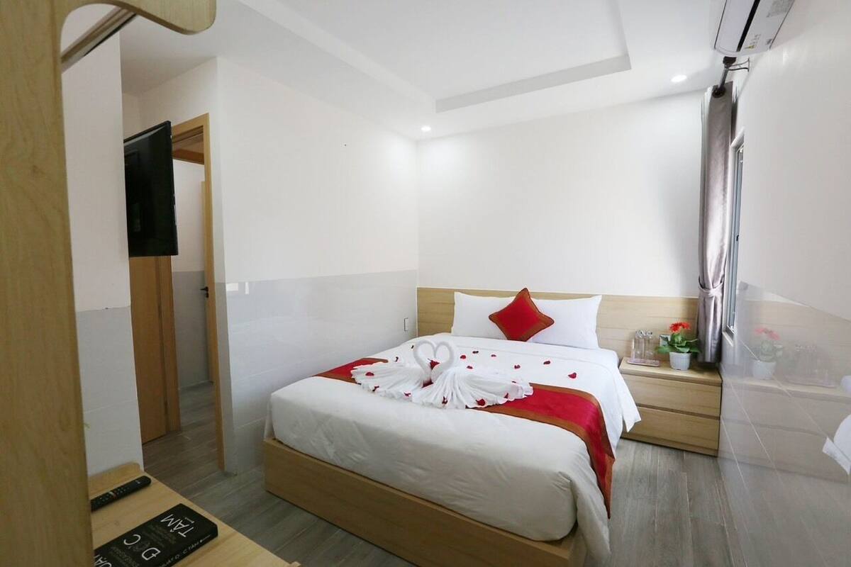 A hotel room with a bed, a bedside table, a TV, and a window with curtains.