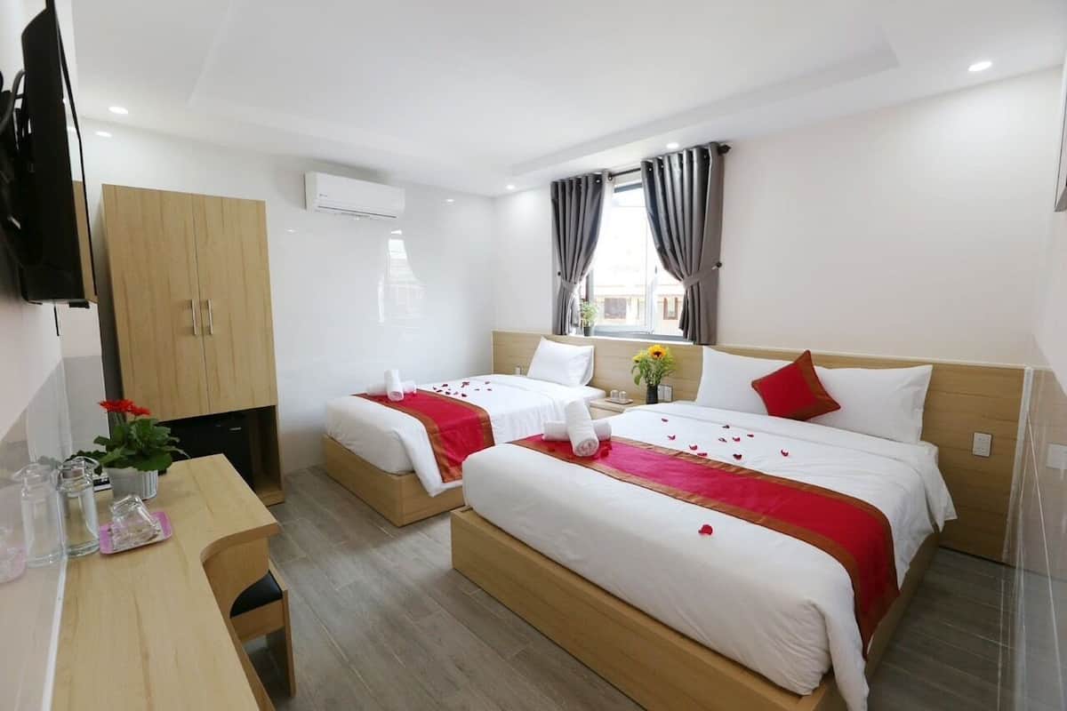 A hotel room with two single beds, a wooden desk, a flat-screen TV, and a window with curtains.