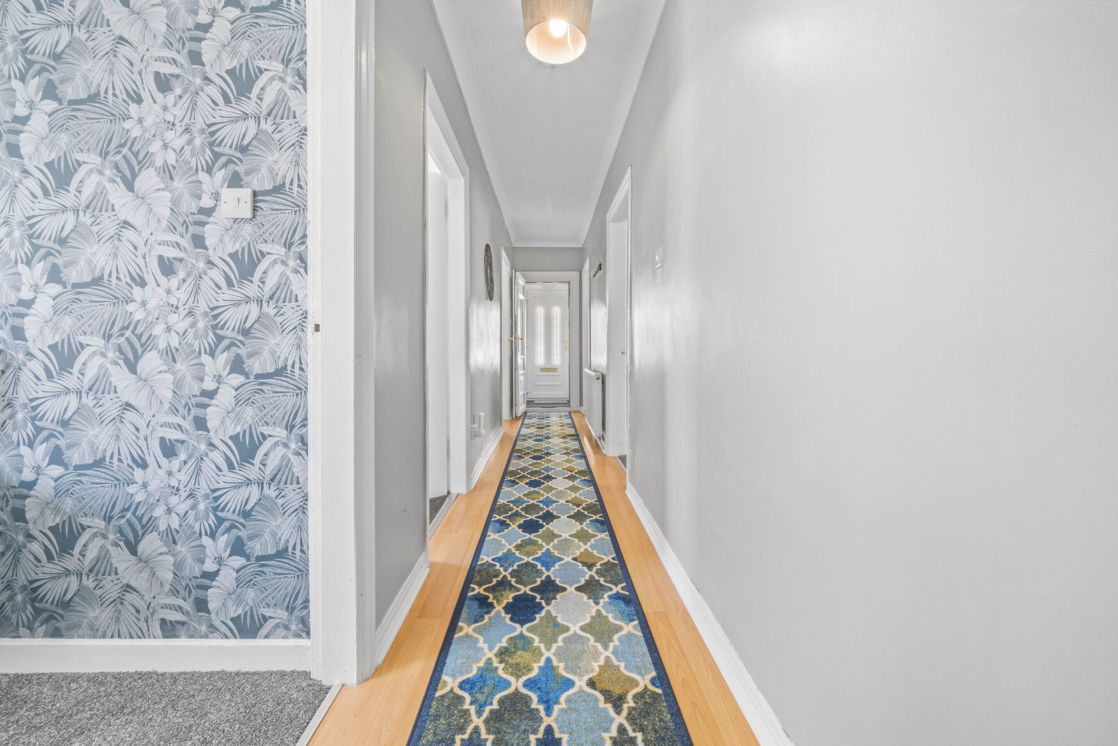 A hallway with a patterned carpet, white walls, and a light fixture.