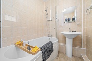 A bathroom with a bathtub, a sink, and a mirror. There are rubber ducks on the edge of the tub.