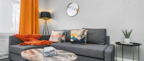 A modern living room with a grey sofa, a round coffee table, and a small side table with a plant.