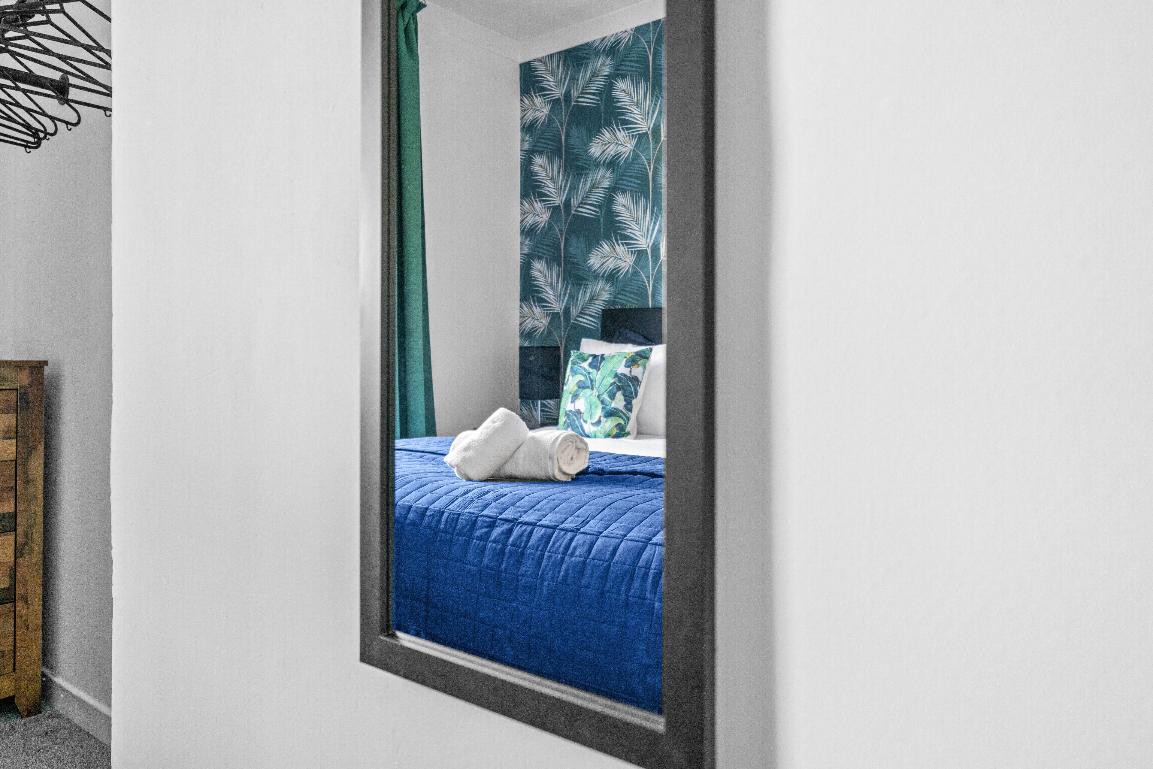 Une chambre à coucher avec un lit, une table de chevet en bois et un miroir qui reflète la pièce.