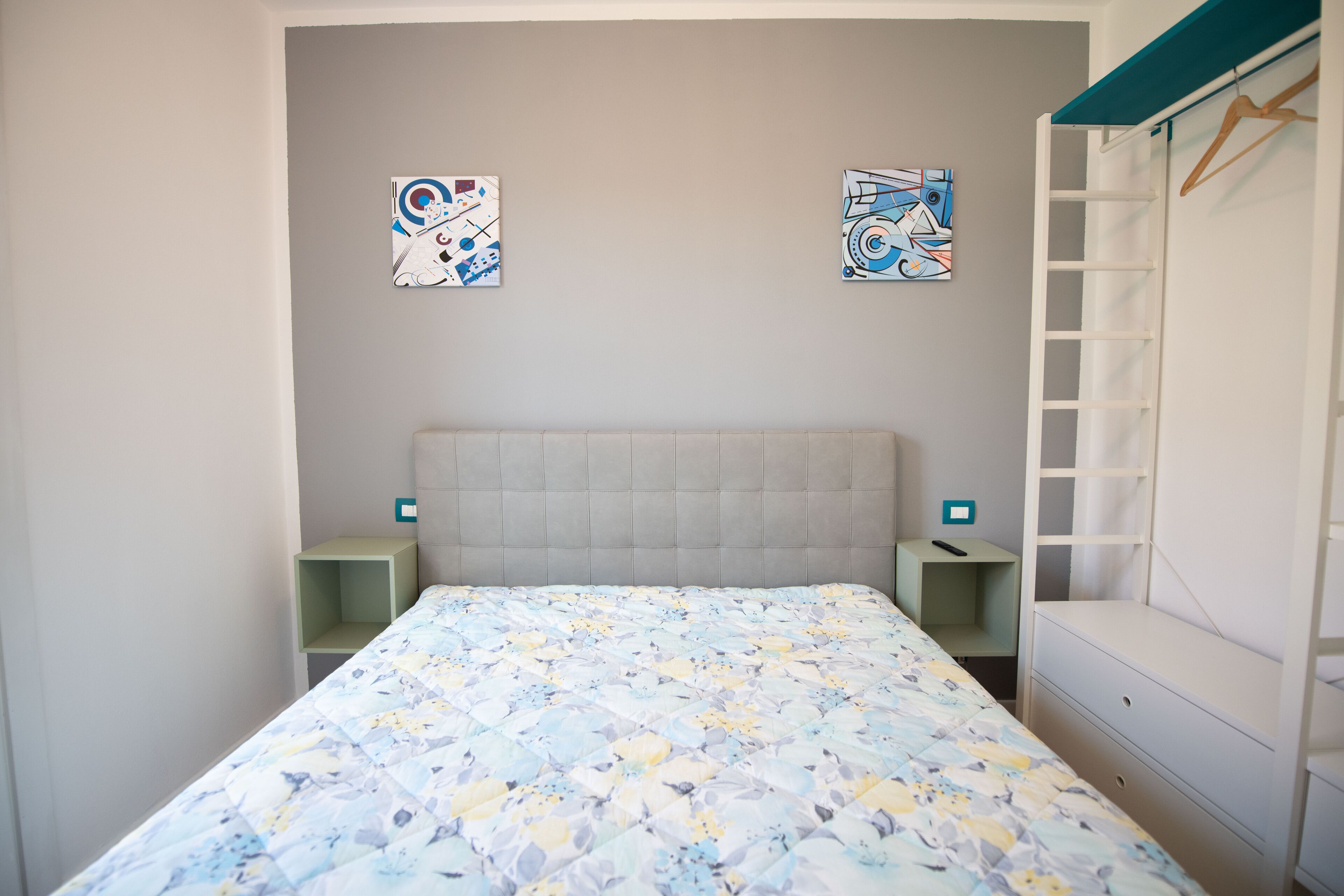 A bedroom with a bed, two nightstands, a dresser, and two abstract wall art pieces.