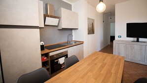 A modern kitchen with a wooden table and chairs, a built-in oven, and a TV on a wooden cabinet. - Appartamento Golf Resort (Manerba del Garda)