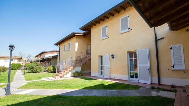 A residential building with a staircase leading to a door, a small garden area, and a clear sky. - Appartamento Golf Resort (Manerba del Garda)