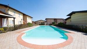 A swimming pool with a tiled deck, surrounded by residential buildings. - Appartamento Golf Resort (Manerba del Garda)
