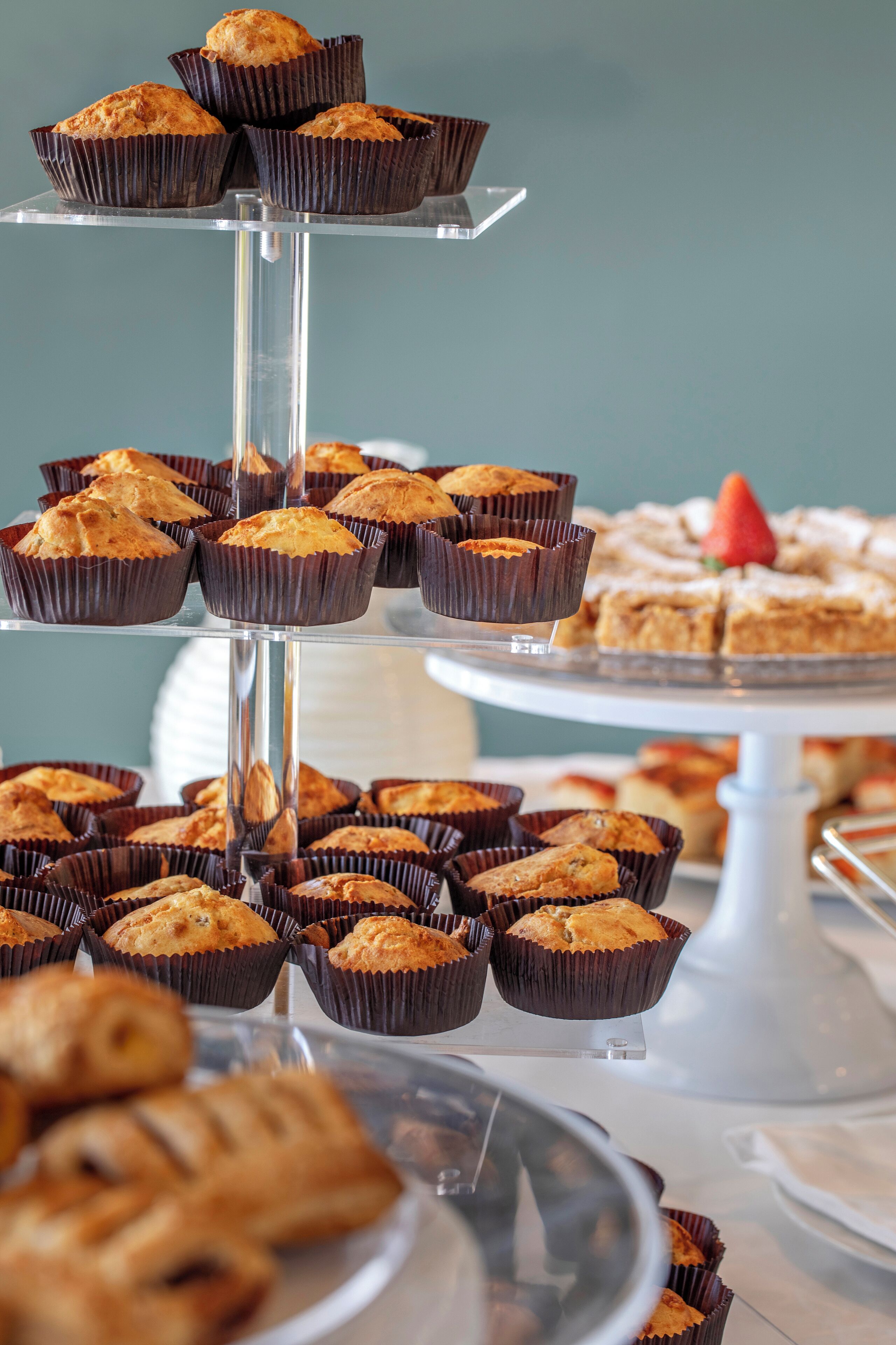 A multi-tiered display of muffins and pastries on a glass stand.