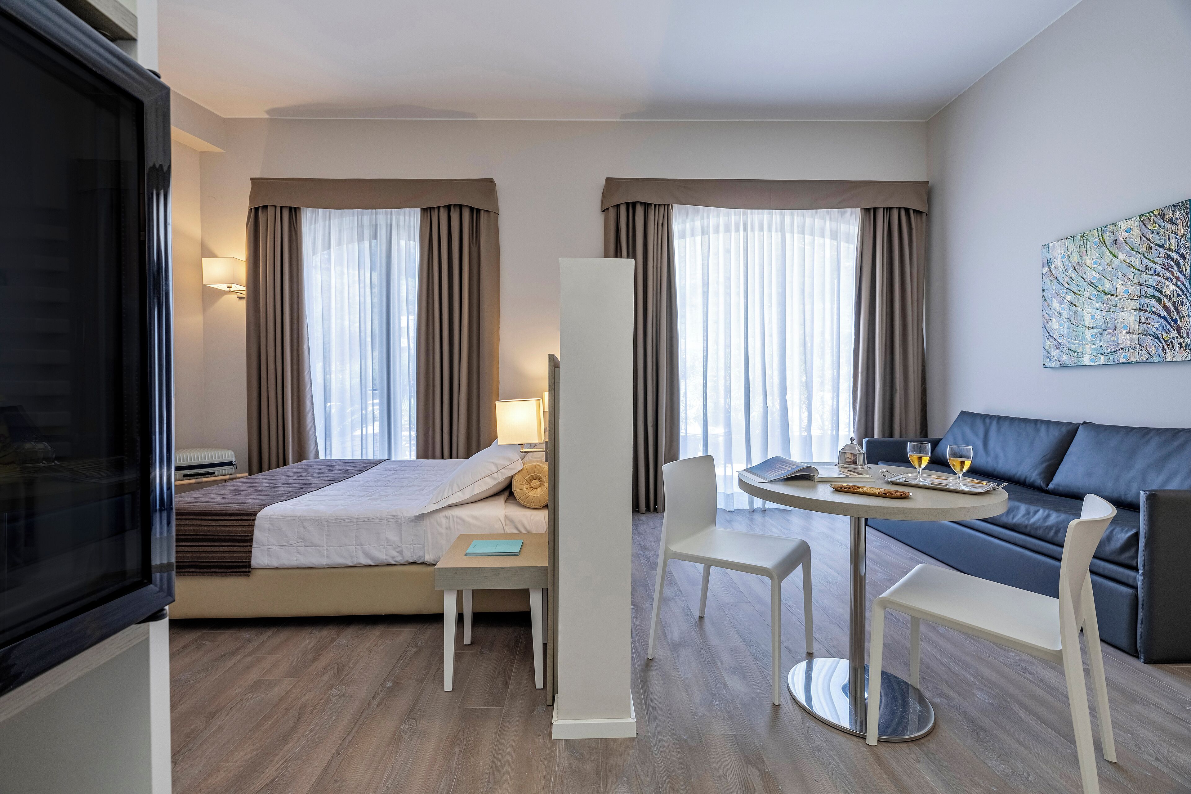 Una camera d'albergo moderna con un letto, un comodino, una lampada e un divano con tavolo e sedie.