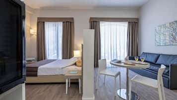 Una camera d'albergo moderna con un letto, un comodino, una lampada e un divano con tavolo e sedie.