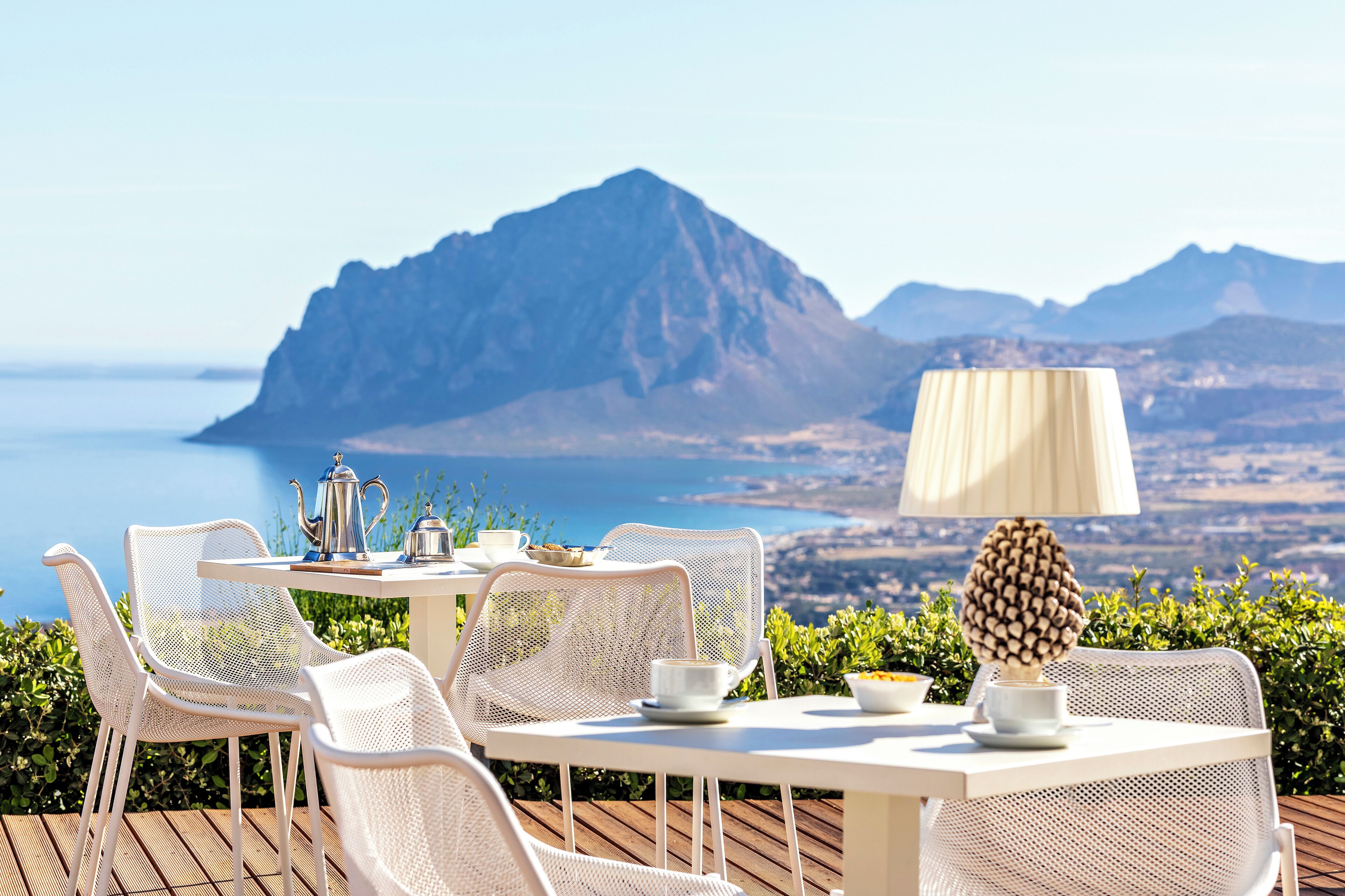 Ein Tisch mit Stühlen und einer Lampe auf einer Terrasse mit Blick auf eine Berglandschaft und das Meer.