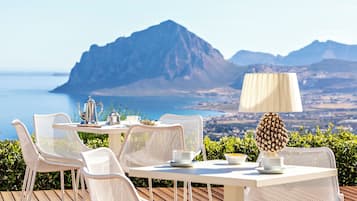 Ein Tisch mit Stühlen und einer Lampe auf einer Terrasse mit Blick auf eine Berglandschaft und das Meer.
