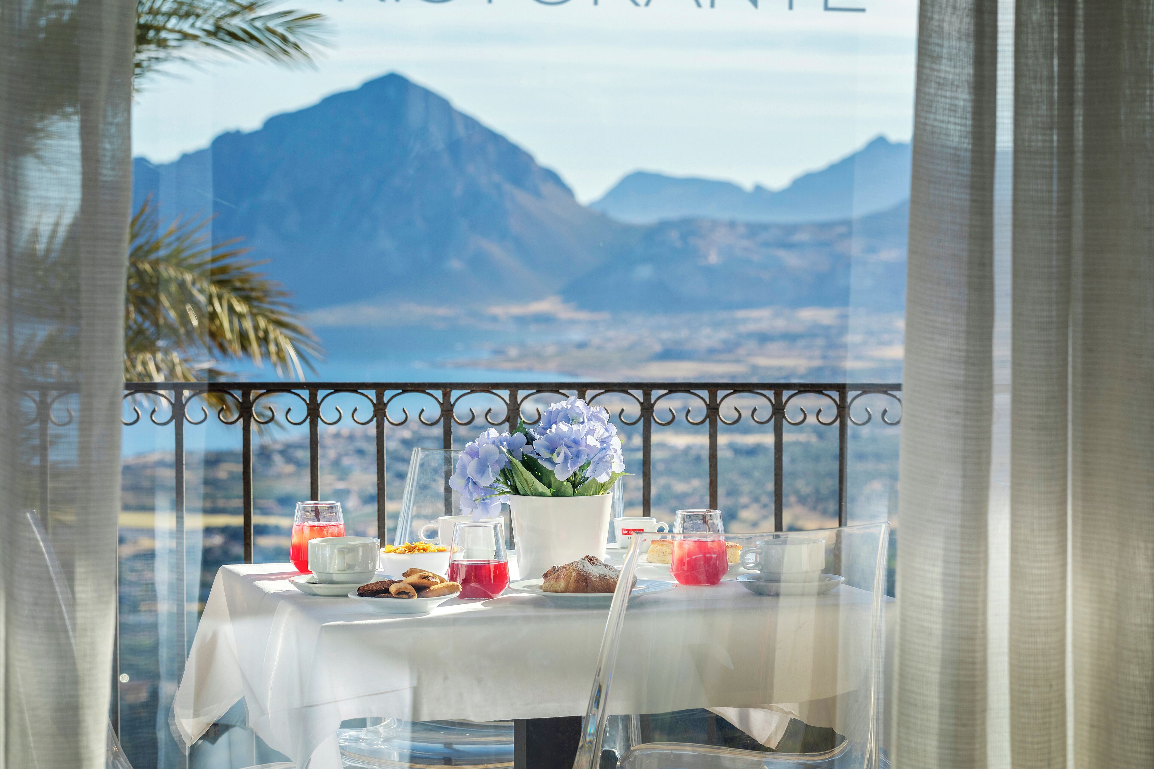 Une table dressée pour le petit-déjeuner, avec une vue sur les montagnes, un vase de fleurs et divers éléments pour le petit-déjeuner.