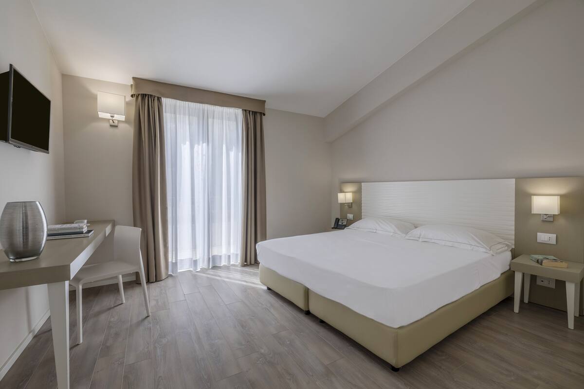 Una habitación de hotel moderna con una cama grande, un escritorio, una silla y un televisor montado en la pared.