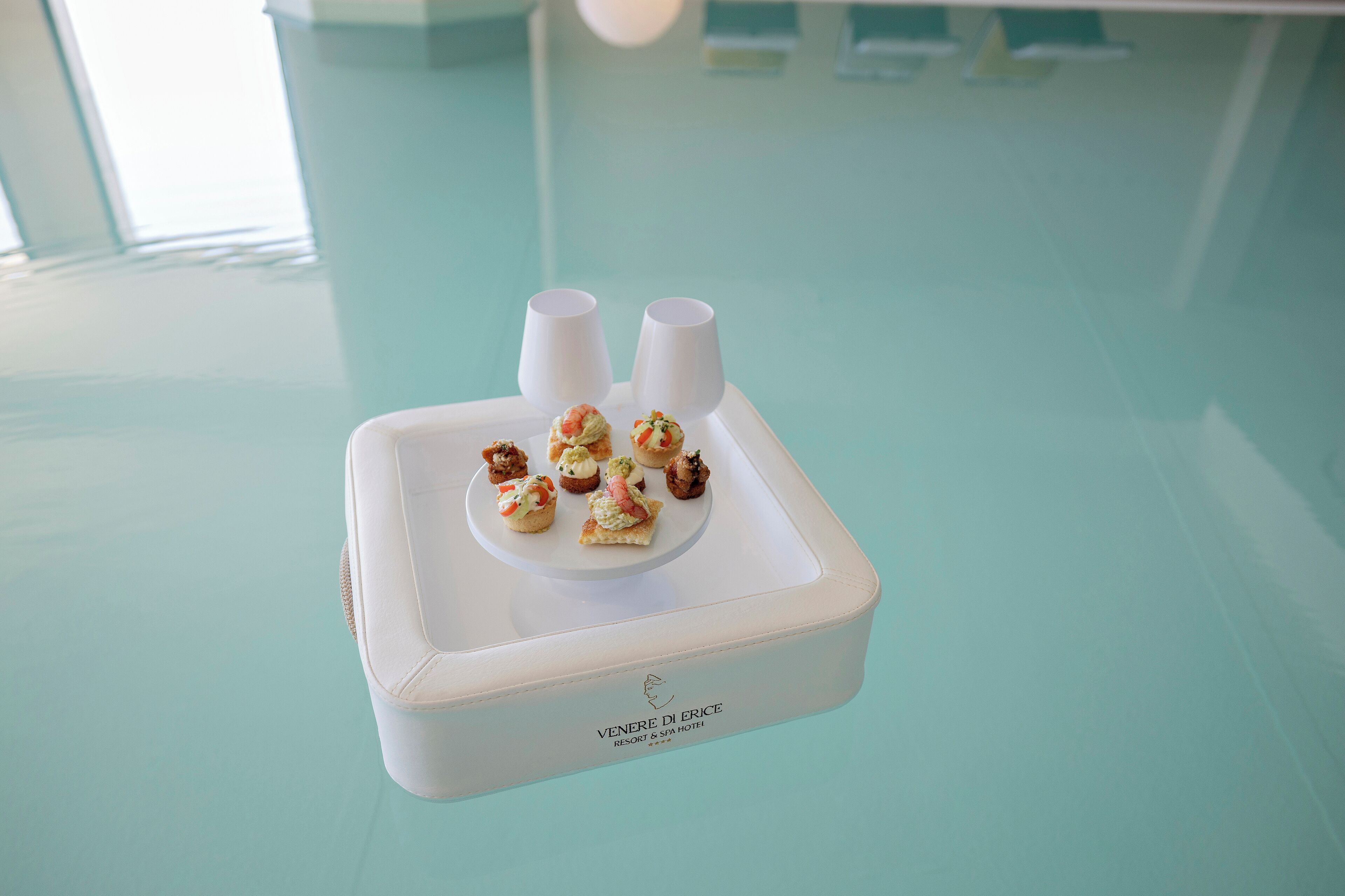 Un plateau blanc contenant de petites pâtisseries et deux tasses blanches, le tout posé sur une surface bleu clair.