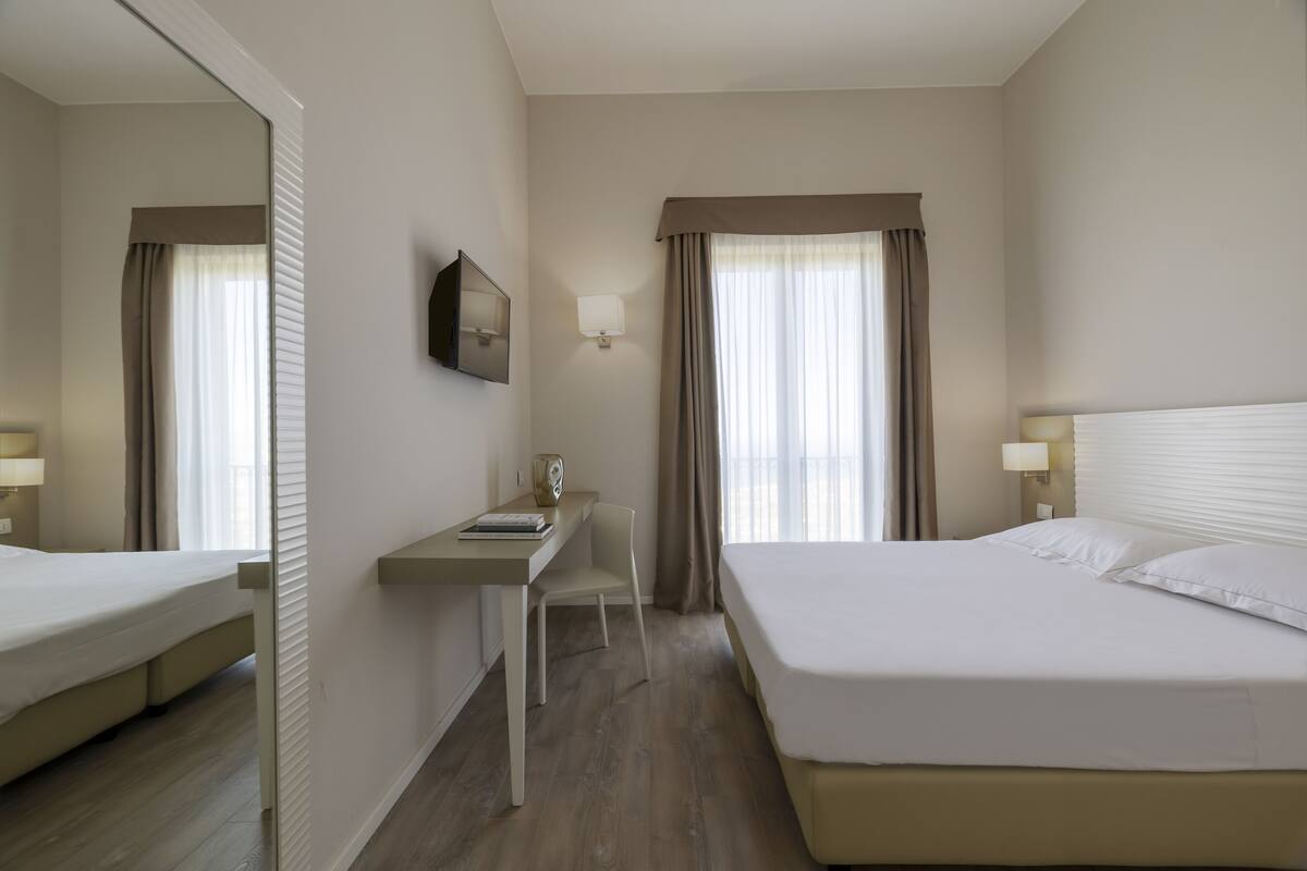 Habitación de hotel con cama, escritorio, silla, televisor y lámpara.