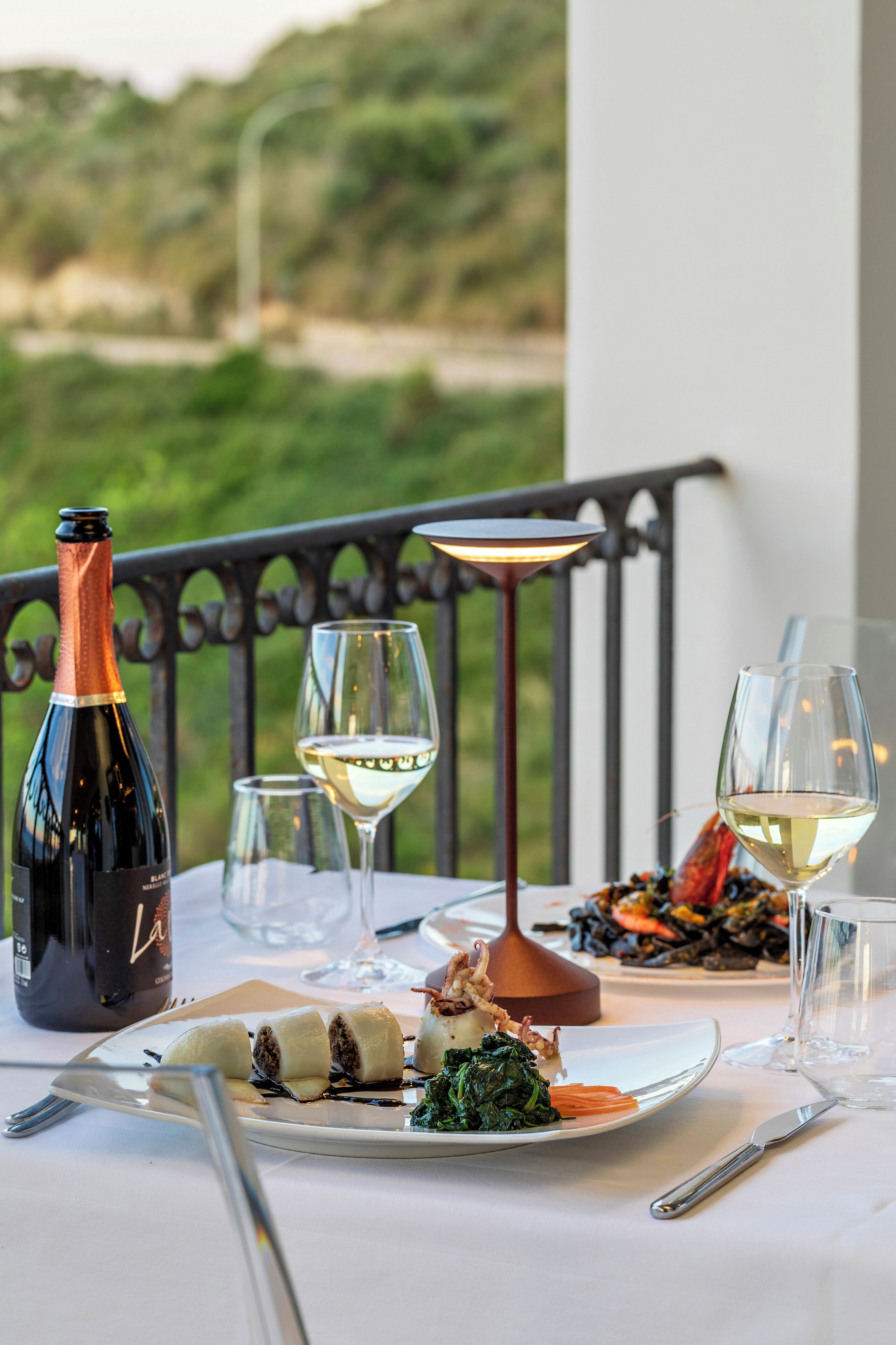 A table set with a bottle of wine, glasses, a plate of food, and a candle.
