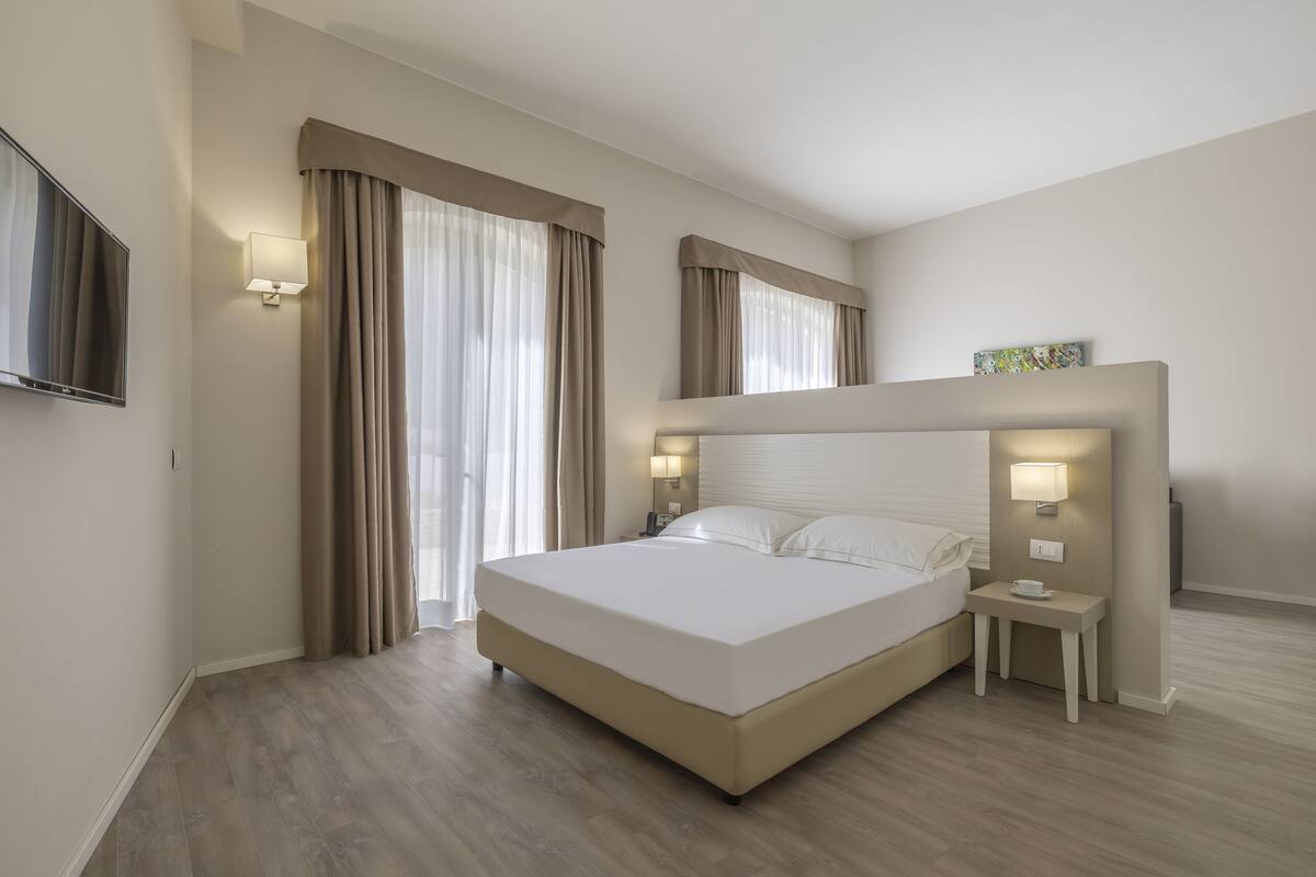 Una habitación de hotel moderna con una cama grande, lámparas de noche, un televisor de pantalla plana y una pequeña mesa con una taza.