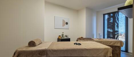 Une salle de spa équipée de deux lits, d’une petite table avec des articles de toilette et d’une grande fenêtre donnant sur un paysage agréable.