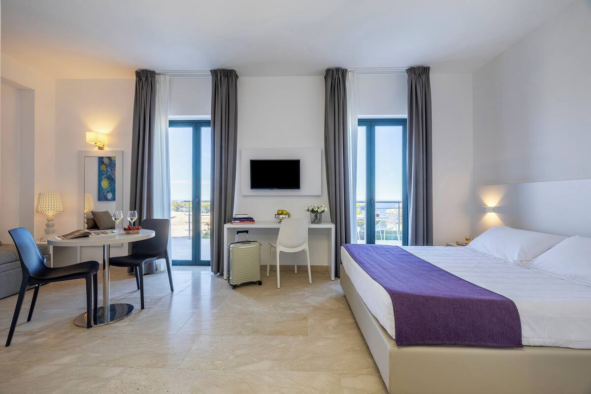Una habitación de hotel con una cama, un escritorio con silla, un televisor y una ventana con cortinas.