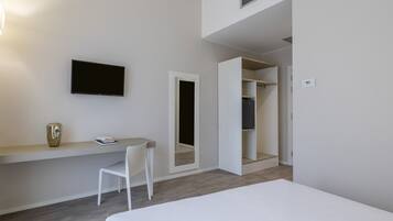 A modern hotel room with a bed, a desk with a chair, a television, and a wardrobe.